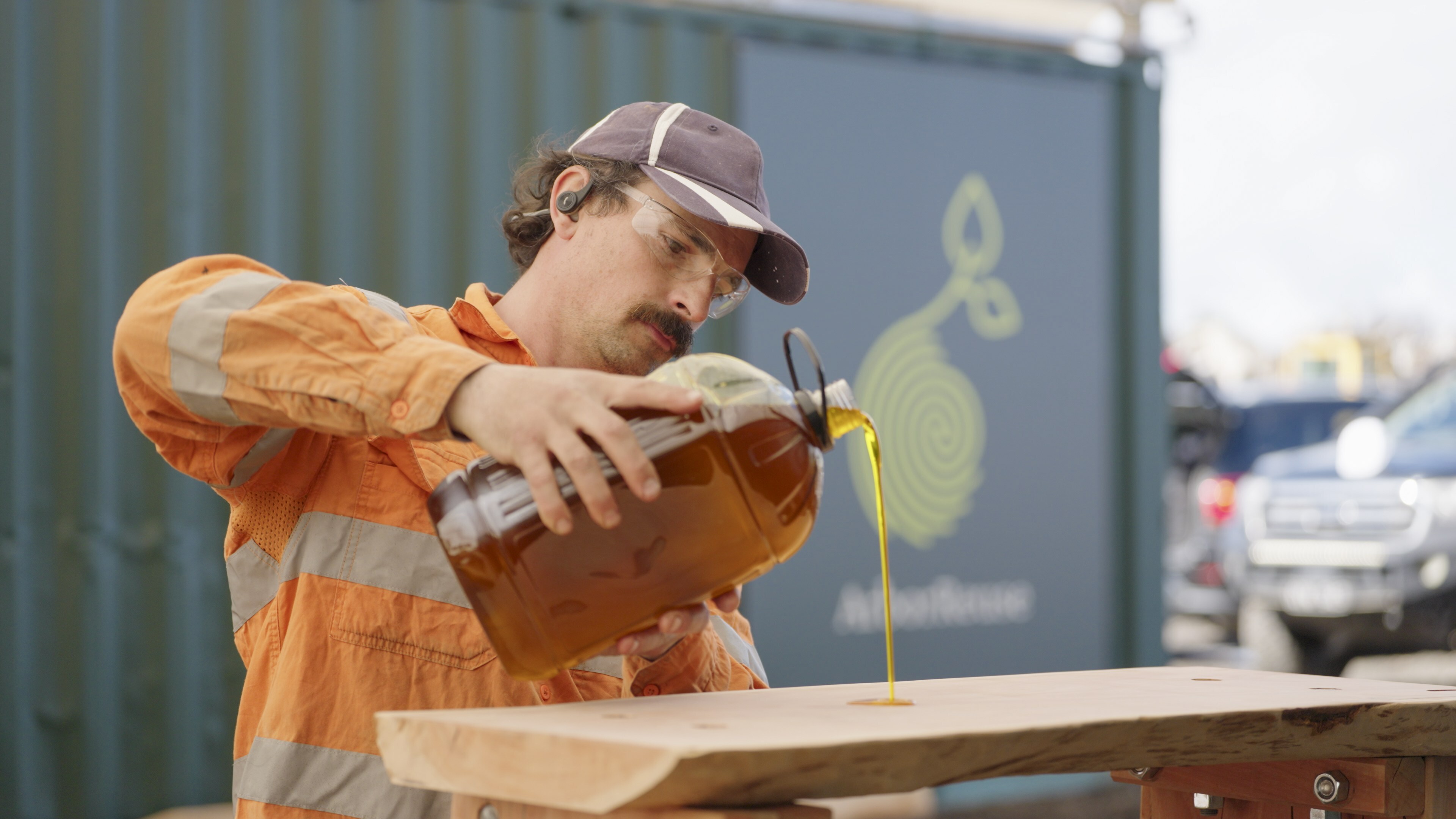 An Arborcraft team member pouring oil finish onto a timber plank in front of the ArborReuse workshop